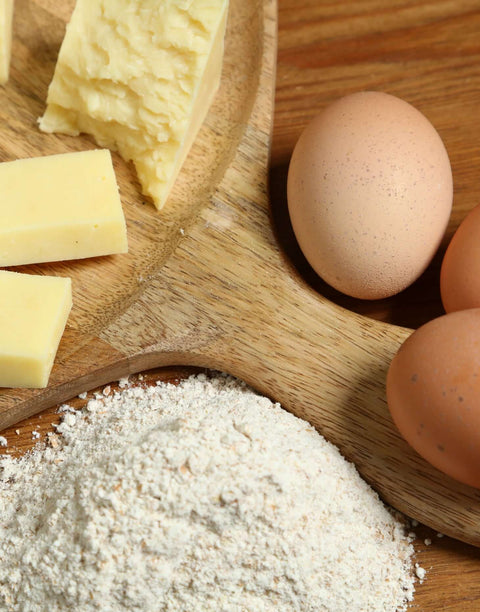Fresh organic cheese, brown eggs, and flour arranged on a wooden board for cooking ingredients.